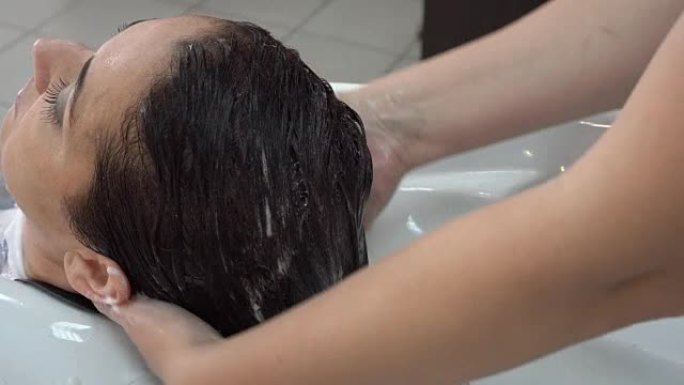 美发师设计师在美容院照顾一个黑发女孩的头发。按摩头发，擦润唇膏。特写，高度细节。