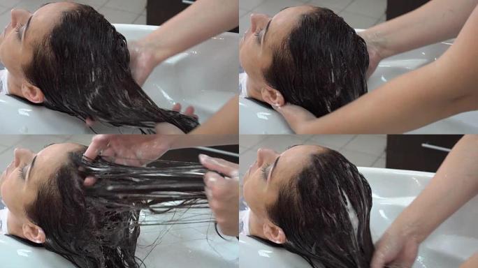 美发师设计师在美容院照顾一个黑发女孩的头发。按摩头发，擦润唇膏。特写，高度细节。