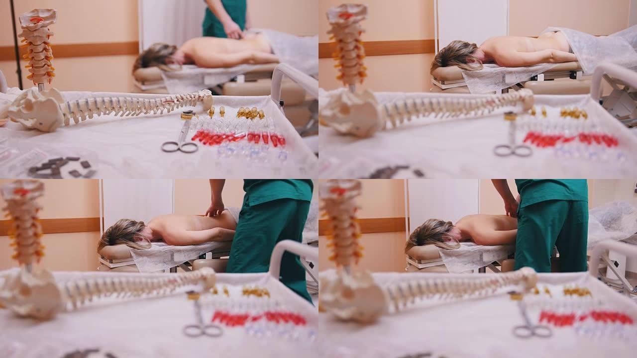 脊椎按摩师按摩一名躺在按摩台上的年轻女子，推动前景中的腰椎、脊柱模型和药物
