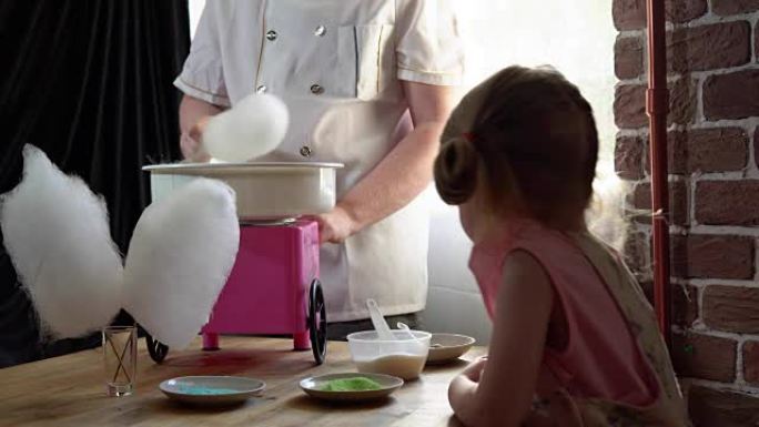一个男厨师在一个可爱的小女孩的专用机器上制作棉花糖。