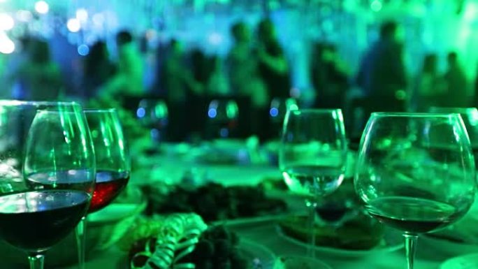 在餐厅或夜总会举行的青年聚会，在跳舞的人的剪影，舞台灯光和紫色填充，浅景深的背景下摆满酒精和食物的宴