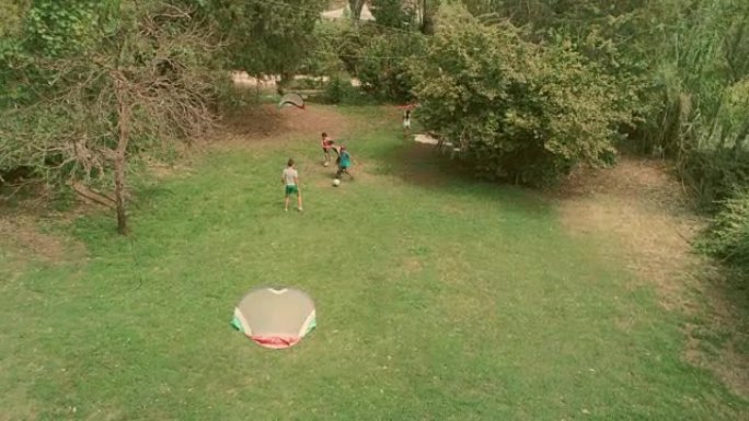 夏令营中快乐的年轻孩子在绿草地上踢足球儿童慢动作空中垂直