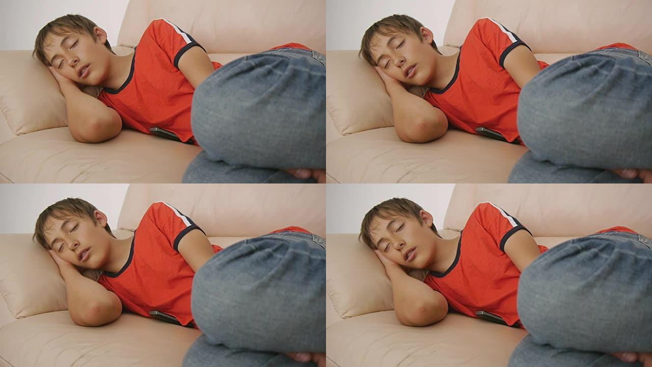 青少年睡在沙发上。白天穿着红色t恤和蓝色牛仔裤的高加索少年男孩睡在米色真皮沙发上。睡眠不足。