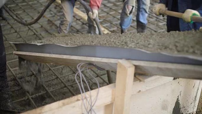 工人正在用混凝土泵将混凝土混合物铺设在钢筋笼子上，以制造建筑物的地板