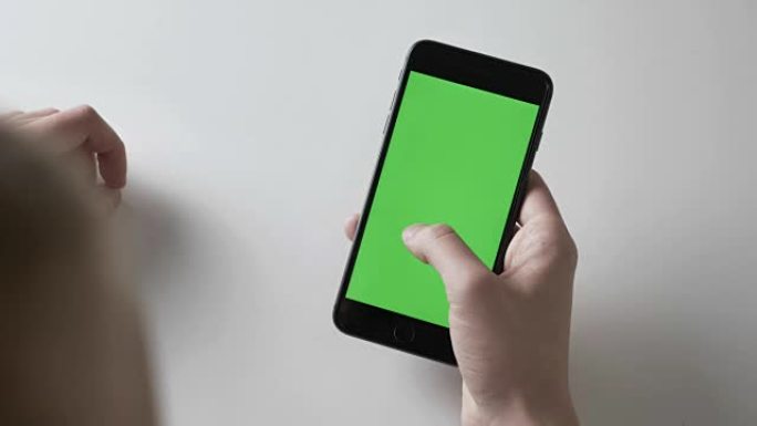男人的双手握着黑色的大智能手机滑动手势。绿色屏幕，chromakey概念60 fps