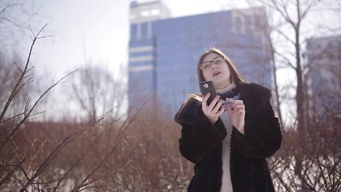 千禧一代白人女孩给她在城市的朋友发短信。年轻的白人妇女在冬季在城市中心打电话给乘车共享