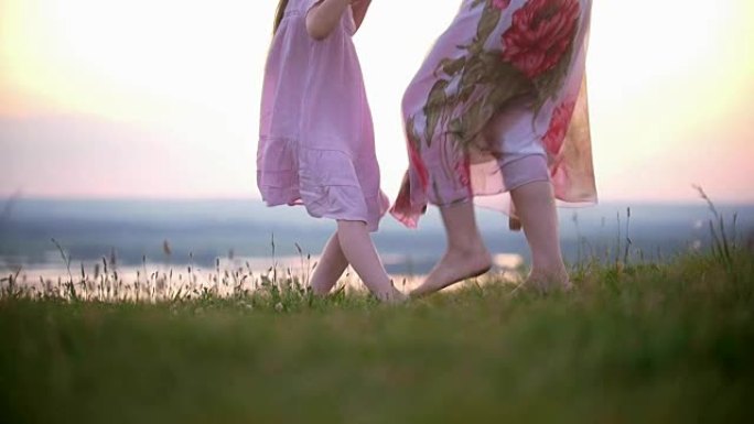 可爱的小女孩牵着妈妈的手在日落的草山上跺脚