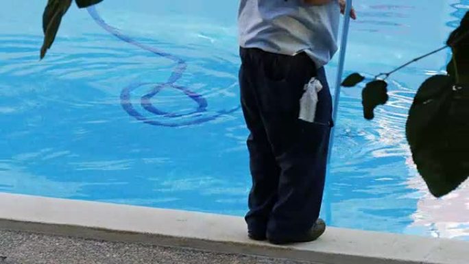 男子以工作形式清洁蓝色游泳池的底部