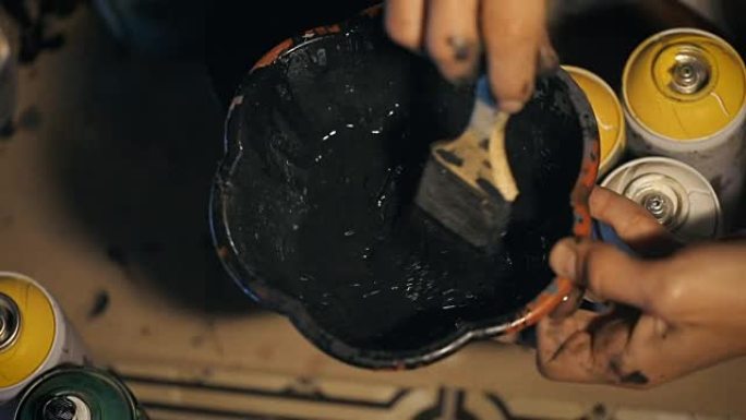 画家用黑色油漆将溶剂倒入碗中，并用刷子将其混合