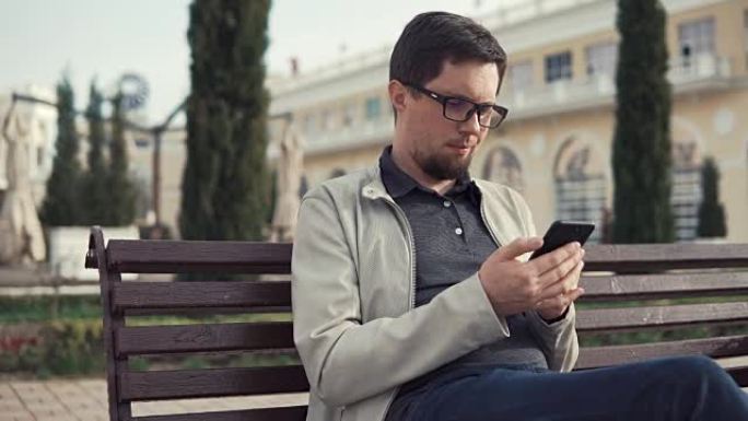 布鲁内特男子坐在公园里用智能手机阅读信息和应答