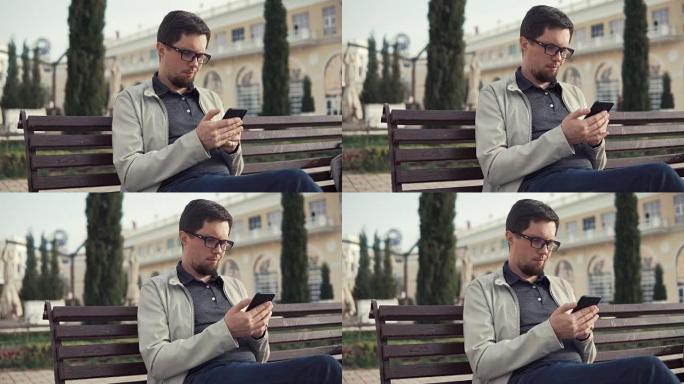 布鲁内特男子坐在公园里用智能手机阅读信息和应答