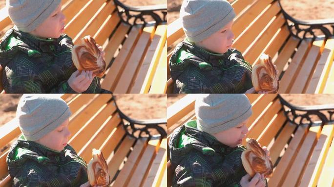 春天，男孩坐在公园的长椅上，吃着加糖的面包。侧视图。