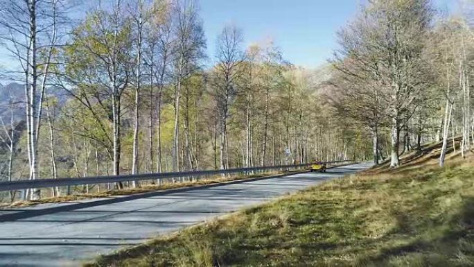 黄色老式汽车在五颜六色的秋天森林中的道路上行驶的向后鸟瞰图。秋天的橙色，绿色，黄色的红树树林。山脉街