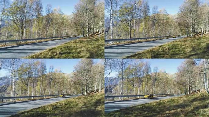 黄色老式汽车在五颜六色的秋天森林中的道路上行驶的向后鸟瞰图。秋天的橙色，绿色，黄色的红树树林。山脉街