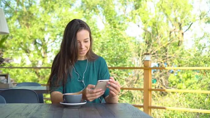 女人拿着智能手机在咖啡馆喝咖啡，微笑着用手机发短信。美丽的年轻女孩的肖像