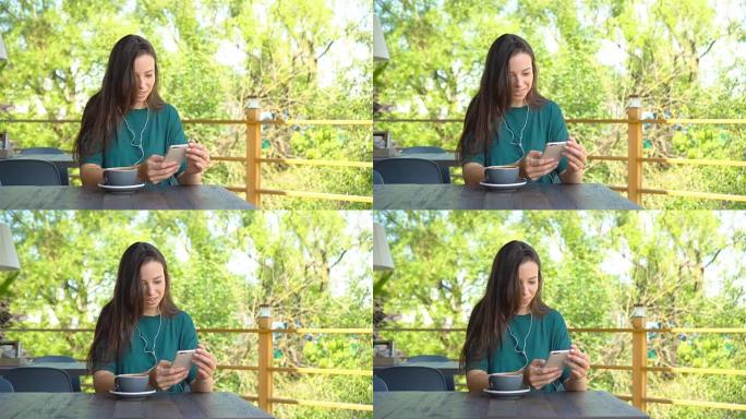 女人拿着智能手机在咖啡馆喝咖啡，微笑着用手机发短信。美丽的年轻女孩的肖像
