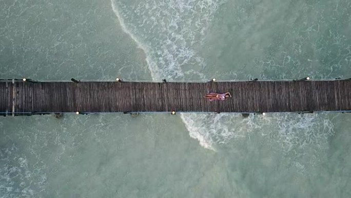 空中: 女孩躺在木桥上。背景上的波浪