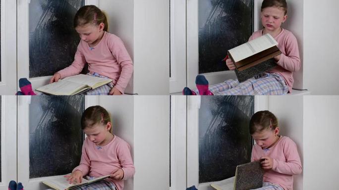 小女孩坐在冰冻的窗户后面的窗台上。可爱的小女孩坐在窗台上，读日记。