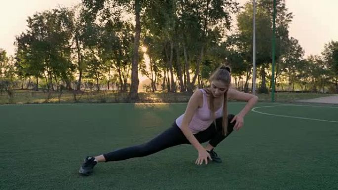 日落时，年轻美丽的女人在公园的足球场上伸展，健身模型锻炼