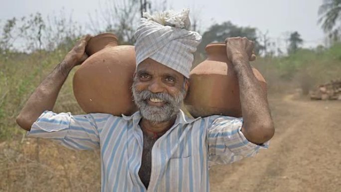 一个快乐而微笑的男性农民，肩上扛着两个装满淡水的土锅