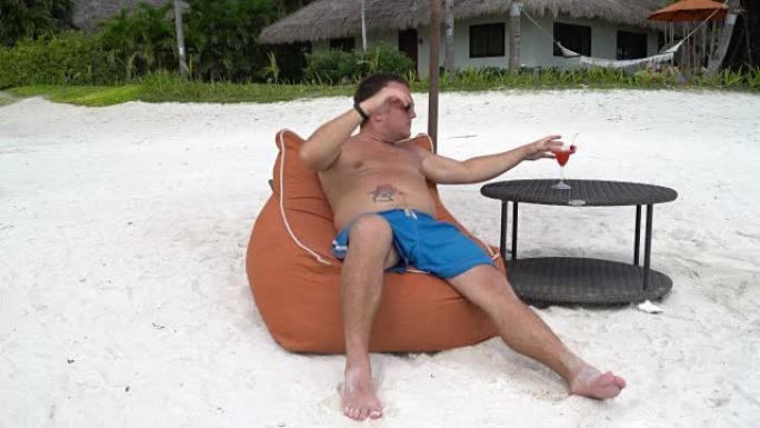 一个男人在海滩上晒日光浴，喝鸡尾酒