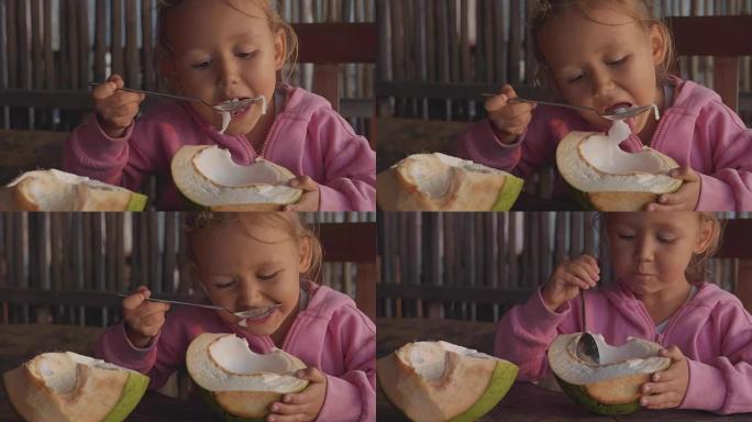 可爱的小女孩在咖啡馆用勺子慢动作吃椰子