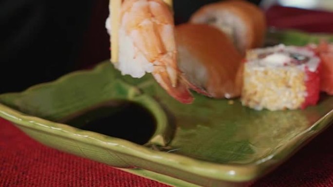 女人在日本餐厅用筷子蘸虾寿司。
