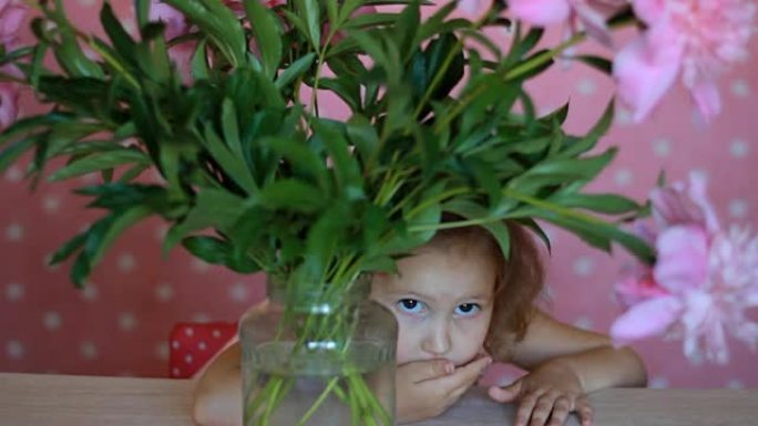 小女孩躲在一个有牡丹的地方。婴儿玩粉红色的牡丹花。
