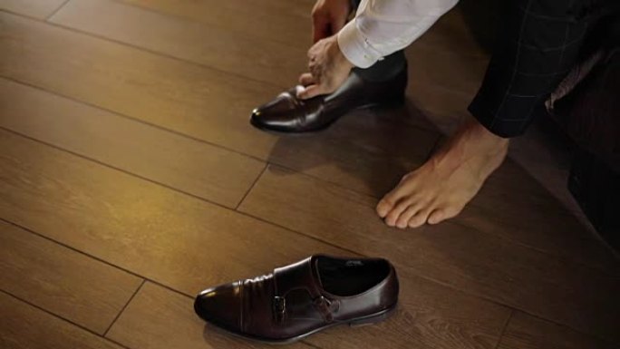 男性双手系紧时尚设计师鞋深色无脸赤脚慢动作。无法识别的男人穿着喜庆的全新鞋子关闭室内自然光商务风格
