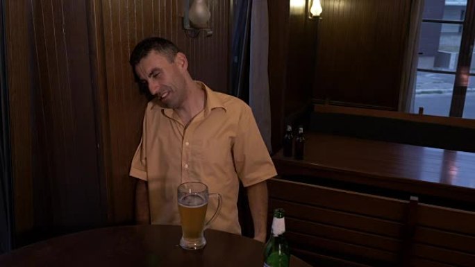 醉汉坐在酒吧的桌子旁喝啤酒