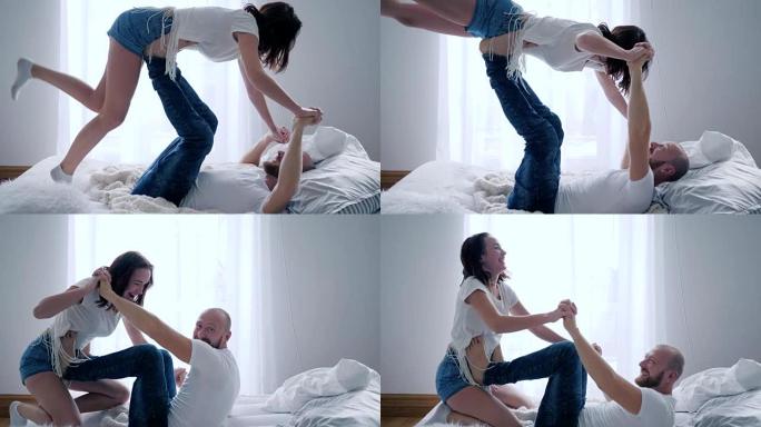 双人练习，微笑的男人举起女孩在家里牵手躺在床上保持双脚平衡