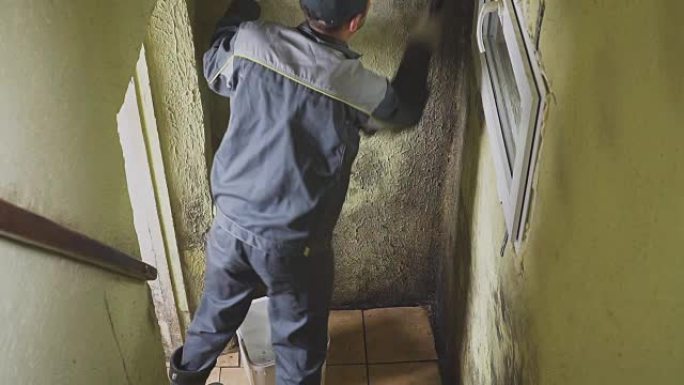 这个人用刷子和抹布清洁墙壁上的污垢。工人手动清洗走廊的墙壁。霉菌和污垢。努力工作