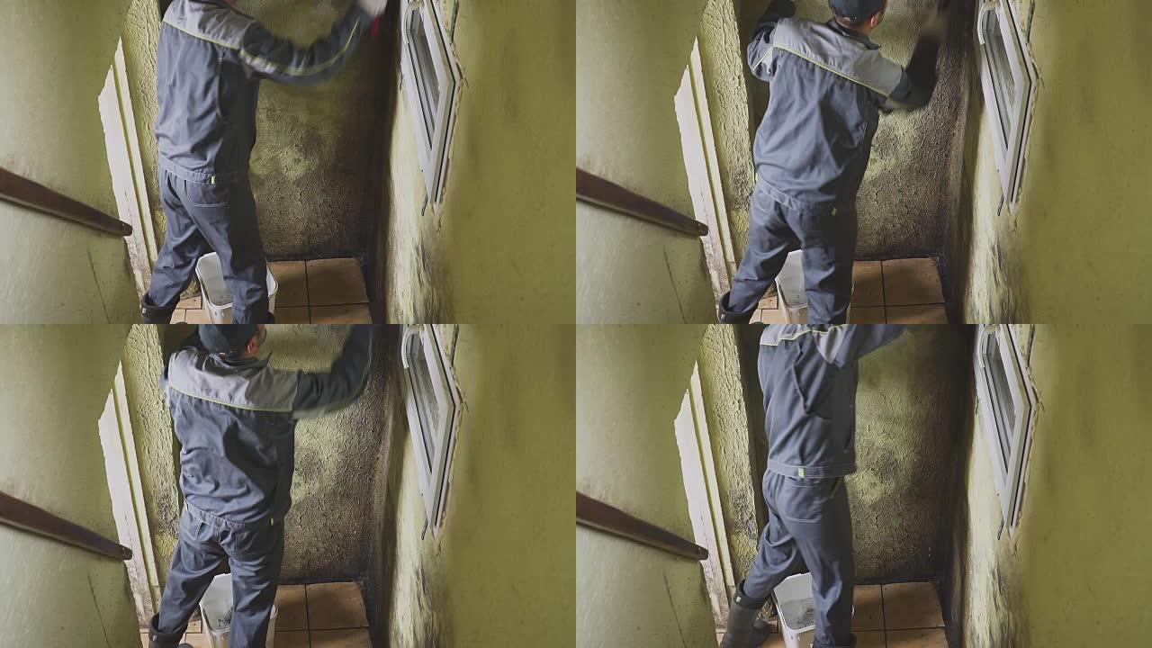 这个人用刷子和抹布清洁墙壁上的污垢。工人手动清洗走廊的墙壁。霉菌和污垢。努力工作