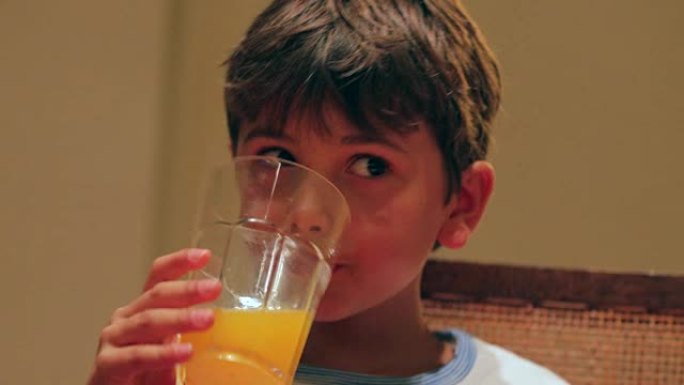 年轻男孩在晚餐时喝橙汁的坦率时刻。儿童在餐桌上喝橙汁