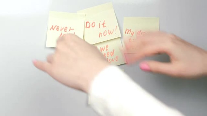 特写女人的手在白板上贴上带有动机短语的黄色贴纸纸。