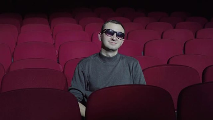 戴3d眼镜的男人坐在黑暗电影院的舒适红色椅子上，看着相机