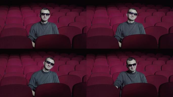 戴3d眼镜的男人坐在黑暗电影院的舒适红色椅子上，看着相机