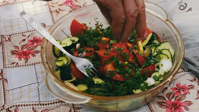 花园里的桌子上有西红柿，梨和蔬菜沙拉。手在给沙拉加盐。健康的蔬菜沙拉。在房子外面野餐。
