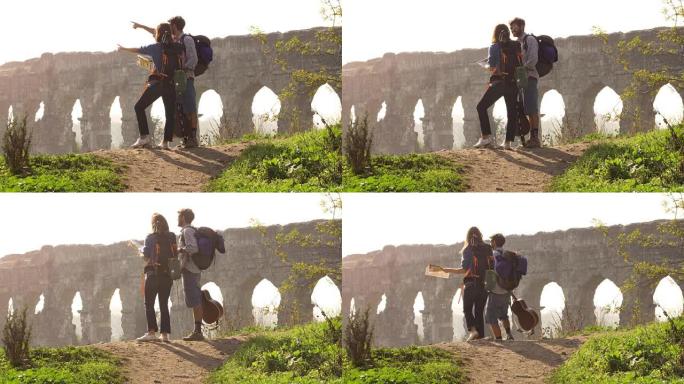 年轻可爱的夫妇背包客游客阅读地图指向罗马渡槽拱门在罗马公园废墟上浪漫的迷雾日出，吉他和睡袋慢动作