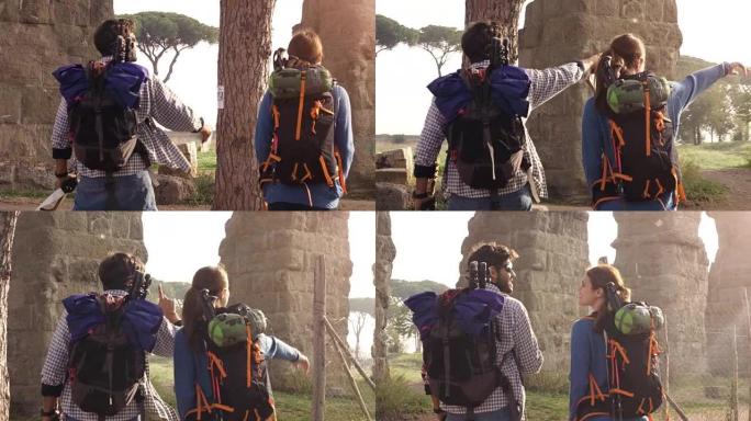 年轻夫妇背包客游客在罗马公园的罗马渡槽拱门附近散步，日出时带着吉他和睡袋慢动作steadycam