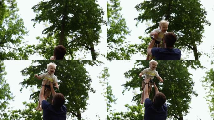 父亲把儿子扔在空中，慢动作。父子俩在绿色公园玩得开心，父亲把小男孩扔向空中。快乐可爱的小男孩。背面视