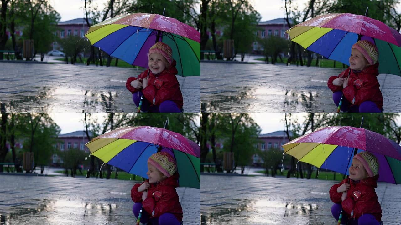 带着五颜六色伞的可爱的小女孩在日落时在公园的水坑里跳跃。