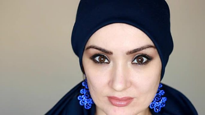 年轻而神秘的阿拉伯女人的脸和眼睛戴着蓝色头巾，被称为头巾，看着相机 .. 一个美丽的现代穆斯林女孩戴