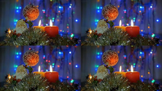 新年和圣诞装饰品。燃烧蜡烛。闪光花环。背景模糊。一个美丽的红球。