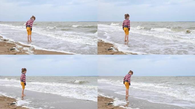 美丽的小女孩看着大海上的海浪站在水面附近。海上弱风暴