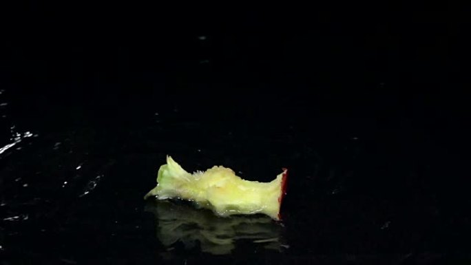 一块苹果掉进水里。黑色背景。慢动作