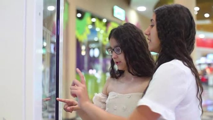 两个女孩使用互动面板在购物中心购物