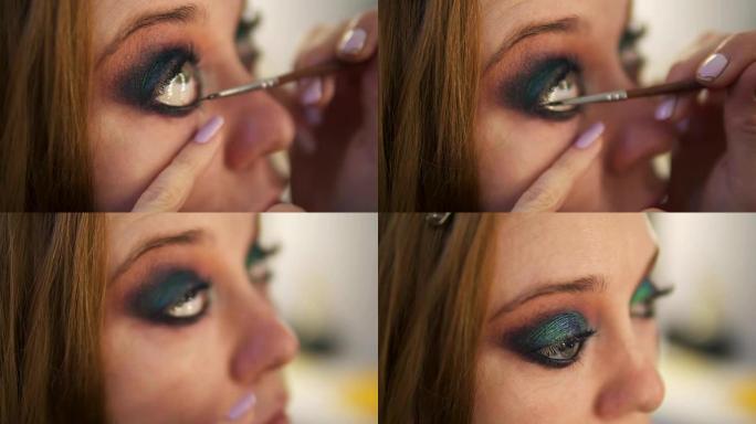 工作室里正在制作年轻女模特的特写镜头。艺术家正在用刷子将黑色眼线涂在右眼下眼睑上。侧视图