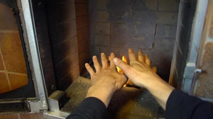 男人在温暖的火炉和温暖的手放松，在城市外的房子里舒适的壁炉