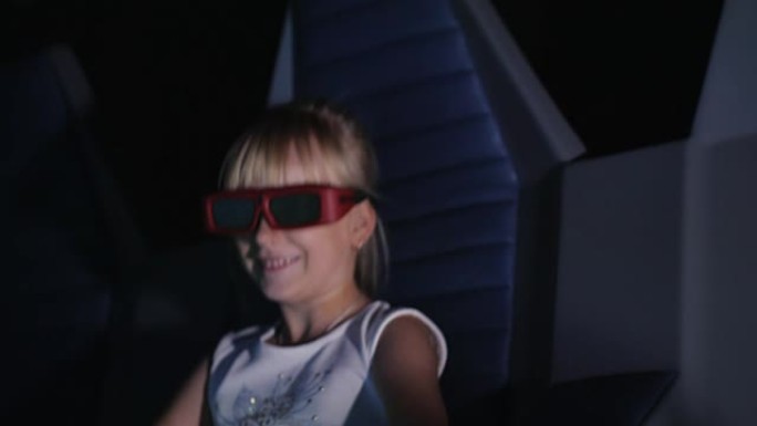 戴眼镜的酷金发女孩在电影院看电影。它吹着风，动感的椅子